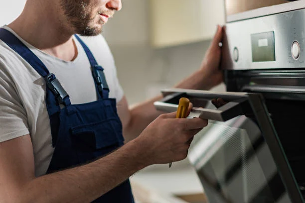 Technician holding a tablet and screwdriver beside a built-in oven