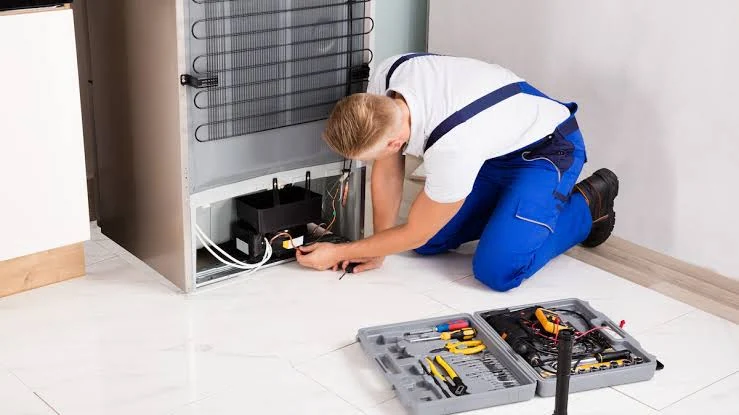 Technician inspecting the compressor at the back of a refrigerator