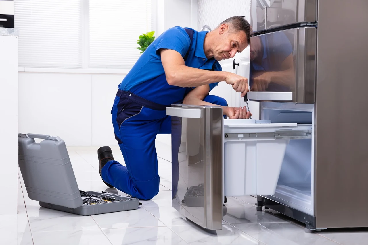 Technician in blue repairing an open refrigerator drawer with a screwdriver
